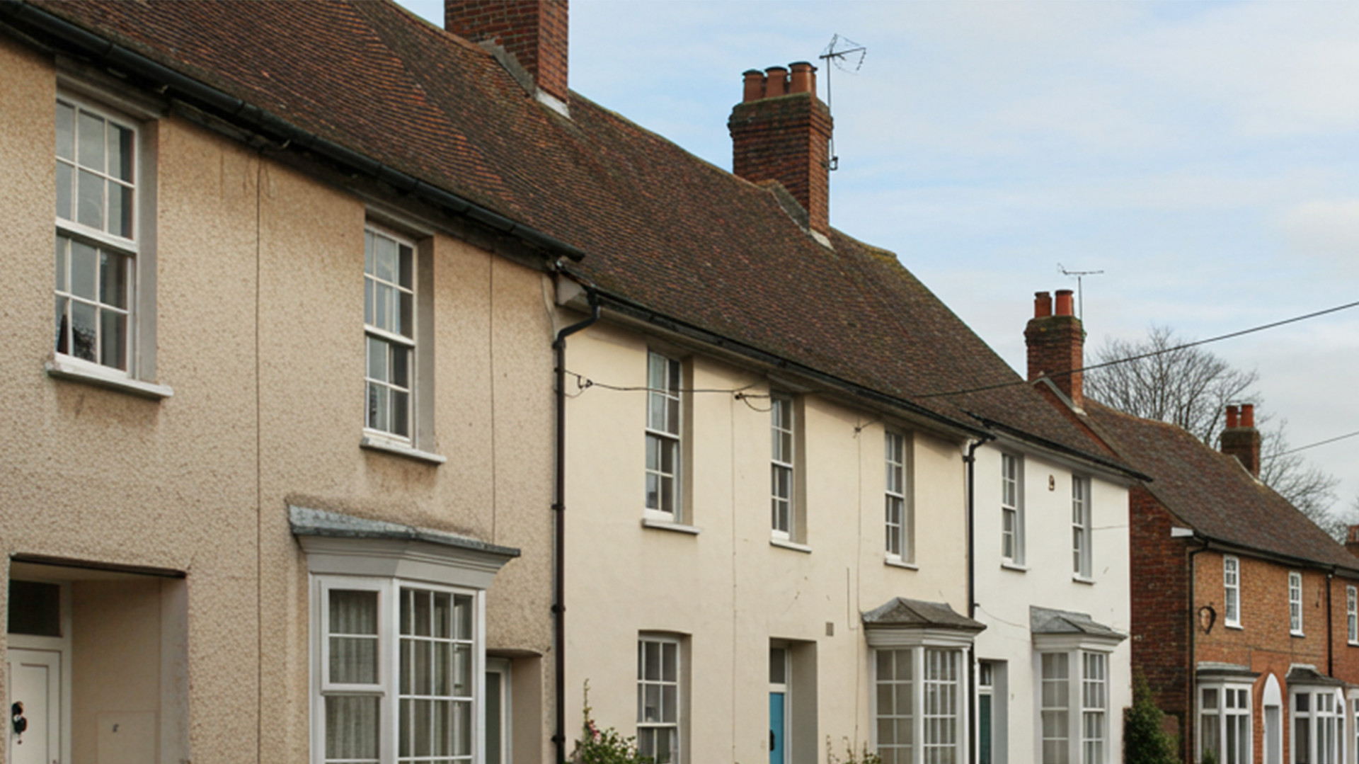 This image shows a street scene in a small town or village. The buildings are mostly two-story houses with a mix of brick and light coloured plaster exteriors.